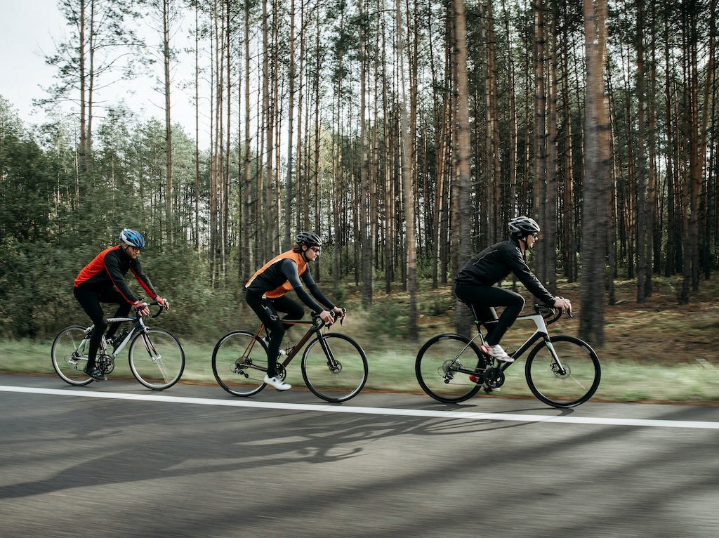 three-people-riding-bikes-on-the-edge-of-a-road-with-trees-in-the-background