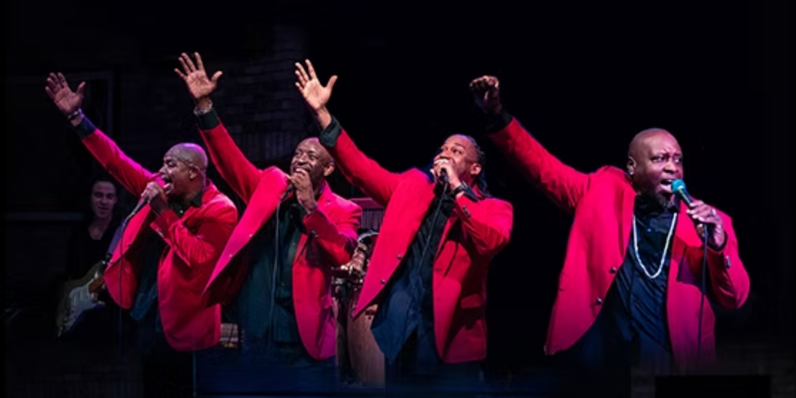 Men of Motown in red costumes with arms in air during a song